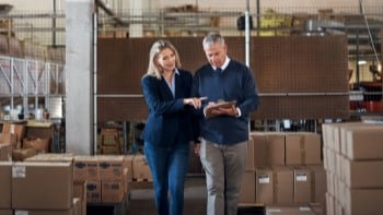 Man and woman in warehouse reviewing clipboard