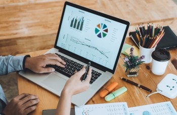 Two business professionals viewing graphs on a laptop and on printed paper