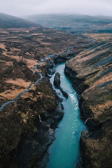 A bright blue river runs through Stuðlagil Canyon with grey clouds above.