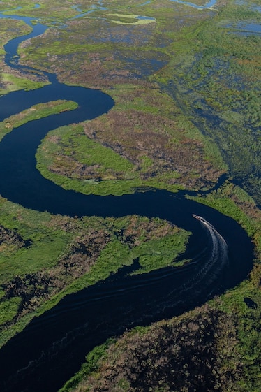 a motorized canoe moves through a windy section of river surrounded by lush green wetlands