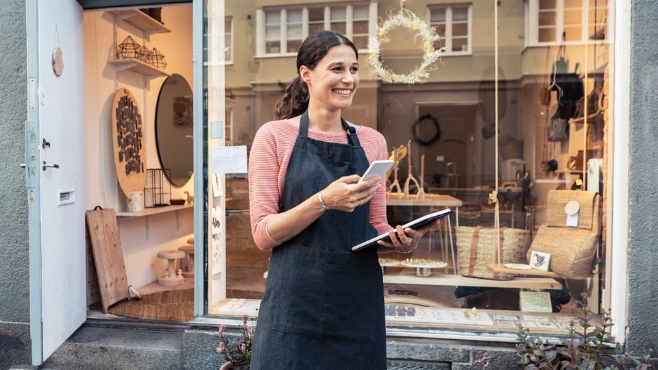 Woman outside her store holding a phone and tablet.