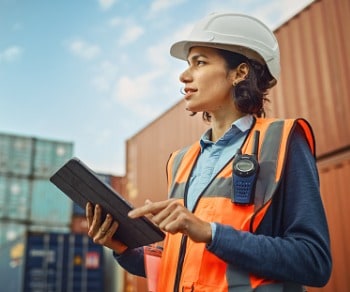 Woman holding tablet surrounded by freight containers