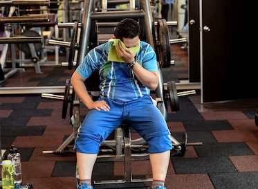 A Malaysian police office wipes sweat from his face as his sits on exercise equipment.