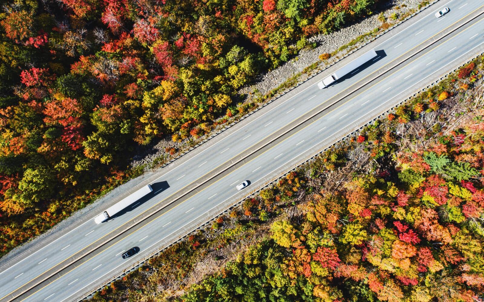 Semi trucks on a highway surrounded by autumn foliage