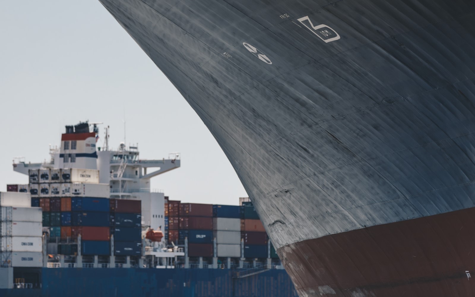 Close up of ship's side with cargo ship stacked with containers in background