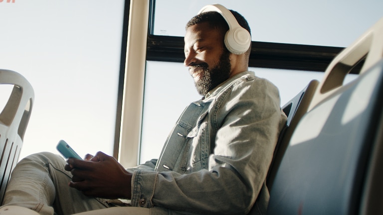 Man sitting on a bus looking at his phone with headphones on