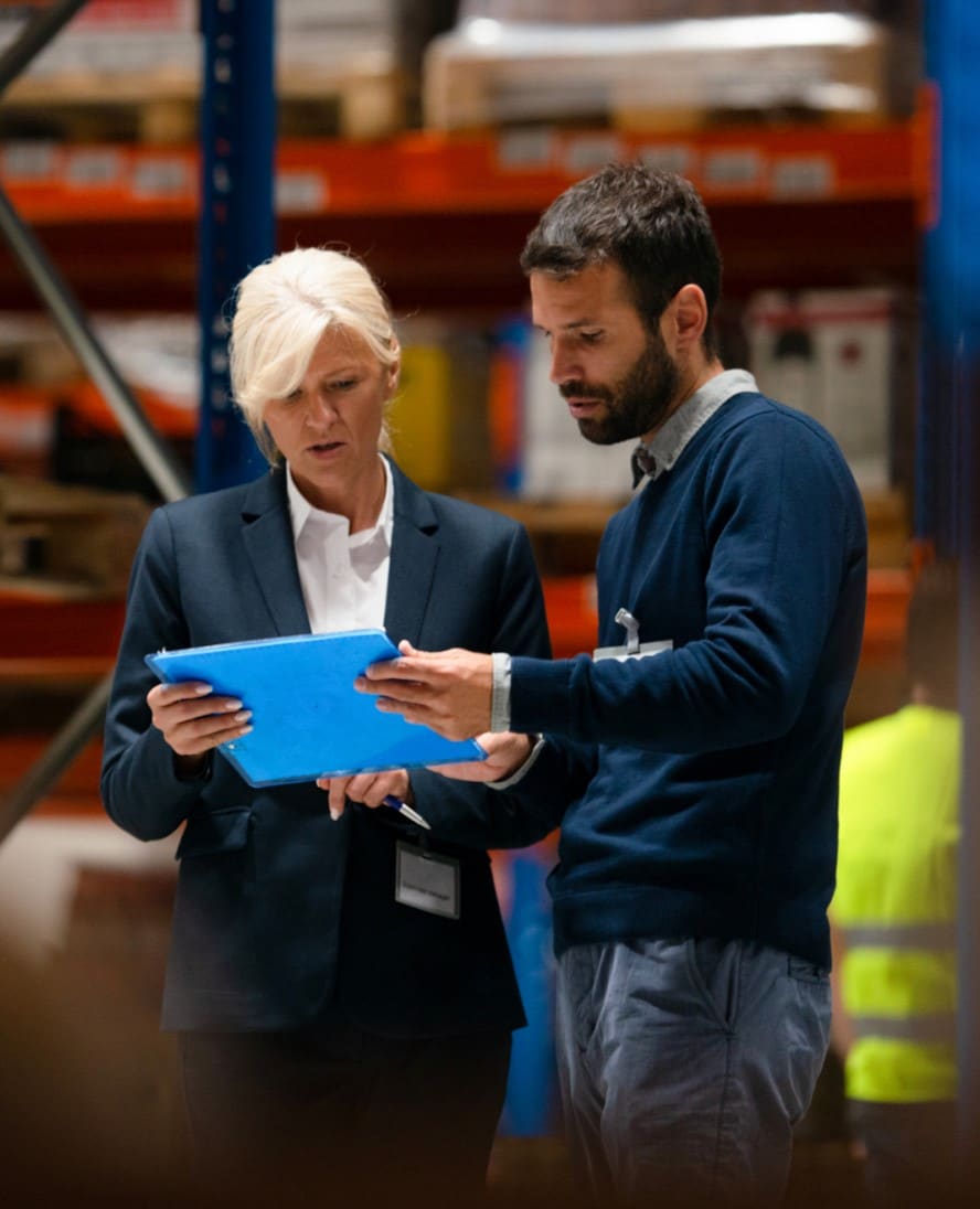 Man and woman in warehouse reviewing paperwork