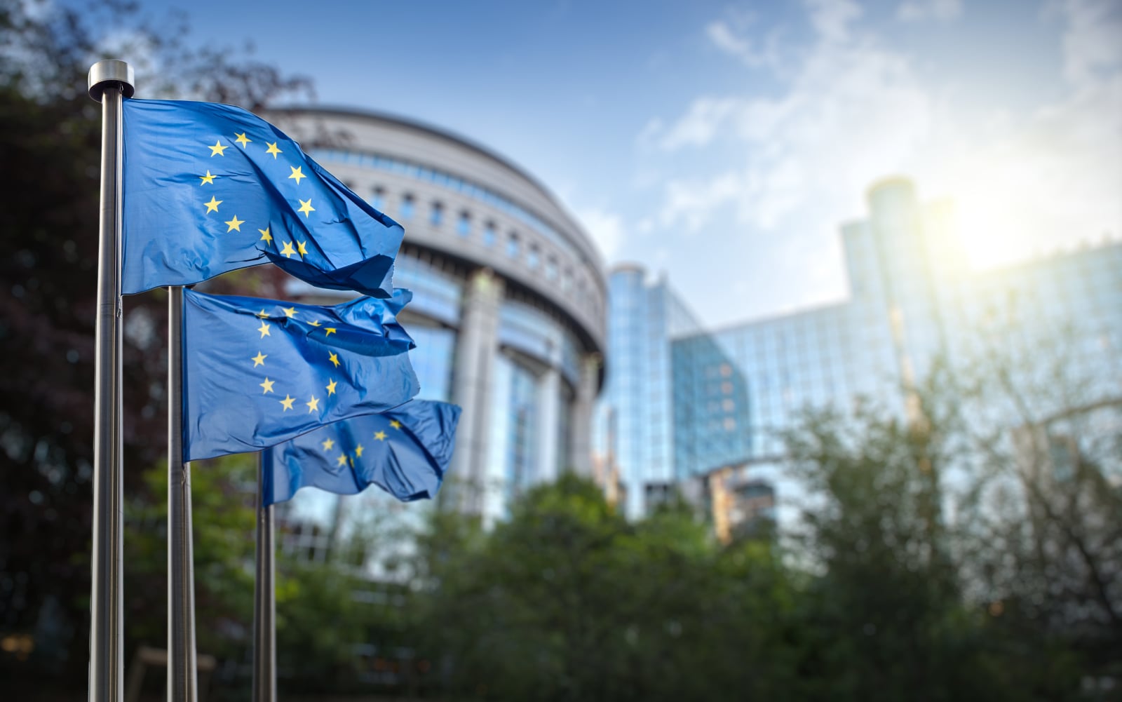 Three European Union flags waving outside of a building