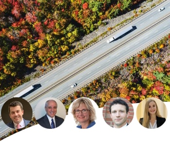 Semi trucks on a highway surrounded by autumn foliage