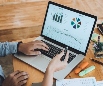 Two business professionals viewing graphs on a laptop and on printed paper