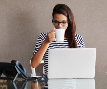 Woman sipping coffee and watching a webinar on her computer