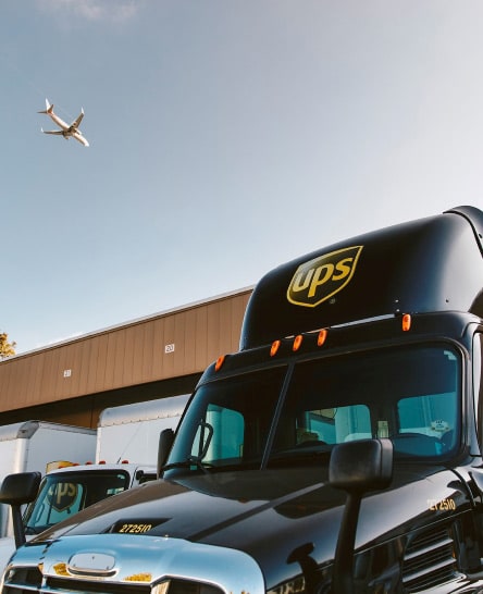 UPS freight trucks at loading dock with jet flying overhead