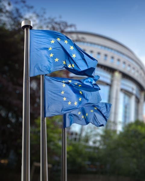 Three European Union flags waving outside of a building