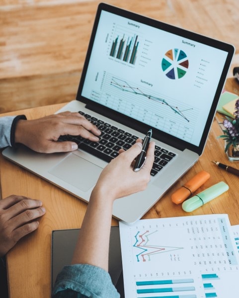 Two business professionals viewing graphs on a laptop and on printed paper