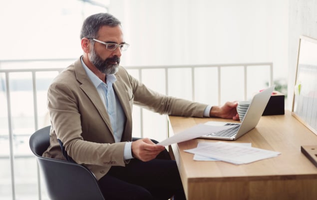 man with glasses looking at paper next to computer