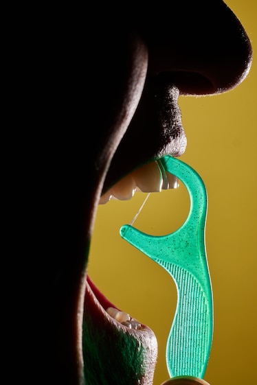 a green floss stick against the teeth of a silhouetted portrait