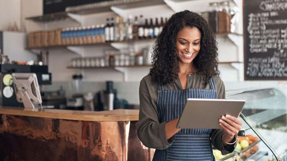 Smiling woman working in restaurant, on tablet. 