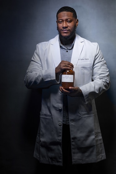 Picture of man in white lab coat holding brown glass jar.