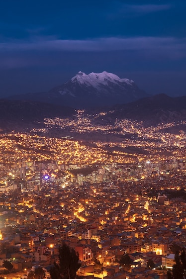 The city lights of La Paz illuminate the area, with the imposing Nevado Illimani in the background.