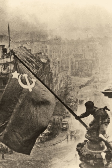 a man holding a Soviet flag over a city turned to rubble