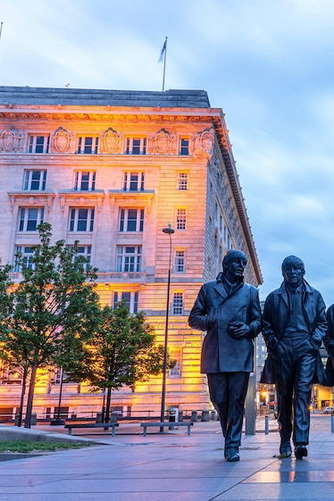 Bronze statues of The Beatles in front of buildings in Liverpool's city centre.